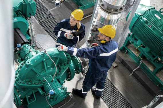 Zwei Ingenieure inspizieren eine große grüne Maschine.